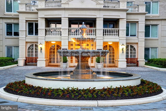 Front view of a building with a decorative fountain in the foreground and arched windows.