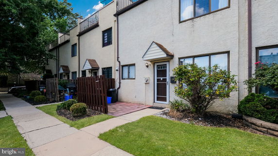 Front view of a townhouse with a small fenced patio and shrubs.
