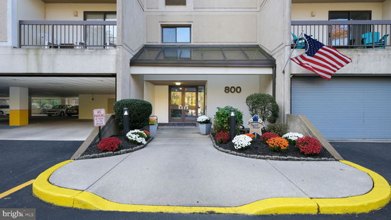 Front view of a building entrance with potted plants and a flag.