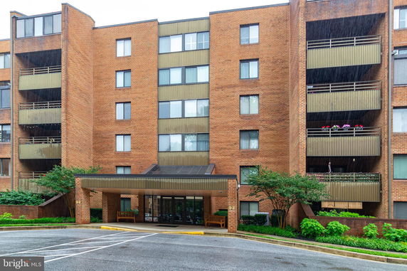 Front view of a brick multi-story residential building with multiple balconies and an entrance canopy.