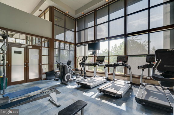 Interior view of a gym area with treadmills, exercise equipment, and large windows.