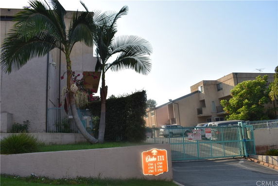 Front view of a multi-story complex with gated entrance and tropical landscaping.