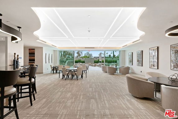 Interior view of a spacious lounge area with tables and chairs, featuring large windows and modern ceiling lighting.