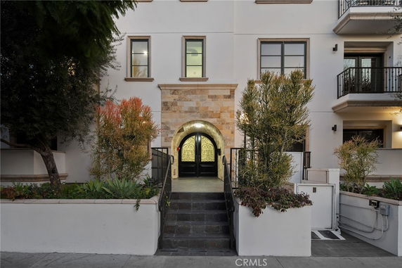 Front view of a multi-story building with arched entrance and surrounding plants.
