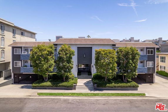 Front view of a multi-story residential building with symmetrical trees and a central entrance.