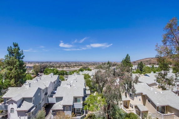 Panoramic view of residential buildings with white roofs and distant landscape under a blue sky.