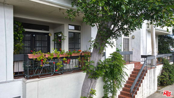Front view of a building with a staircase and a balcony with plants.