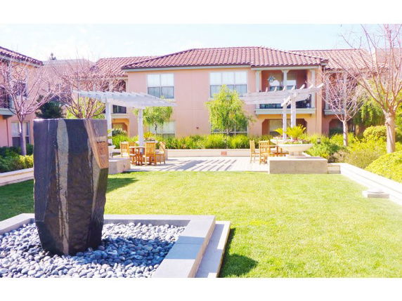 View of a building with a courtyard featuring a stone sculpture and seating area.