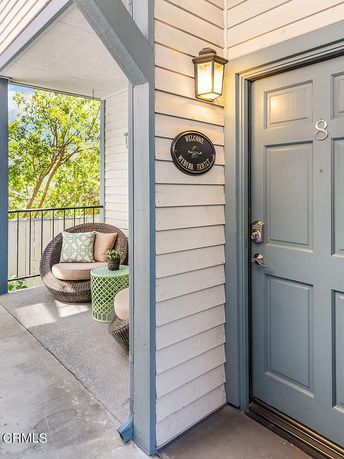 Entryway of a building with a blue door and a welcome sign, accompanied by a small seating area with chairs and a table.