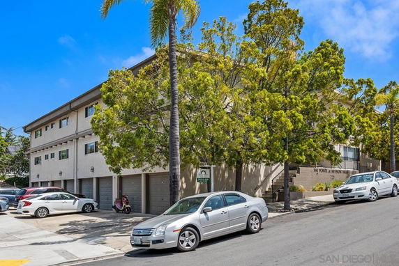 Front view of a multi-story residential building with garages and parked cars.