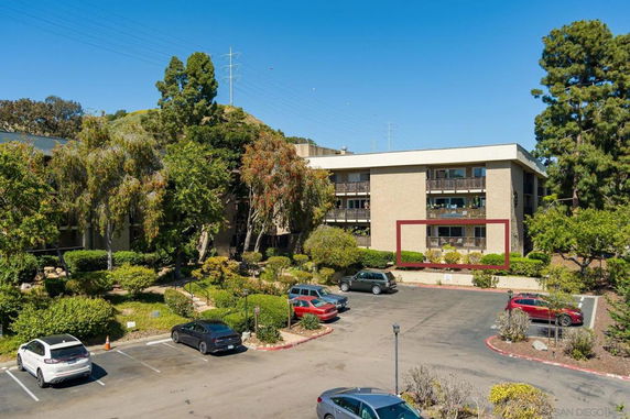 Front view of a multi-story building with balconies and adjacent parking area.