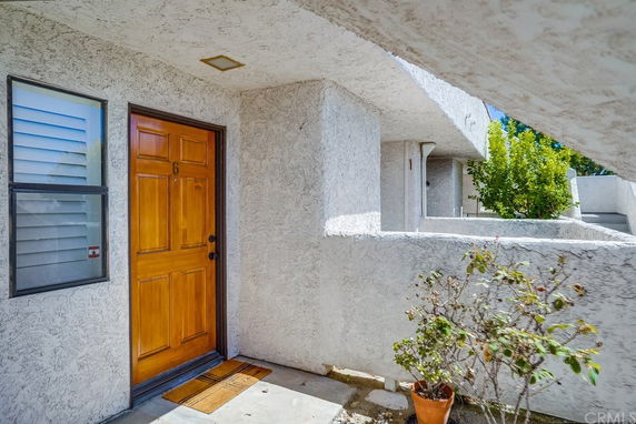 Front view of a residential building entrance with a wooden door and exterior stucco walls.