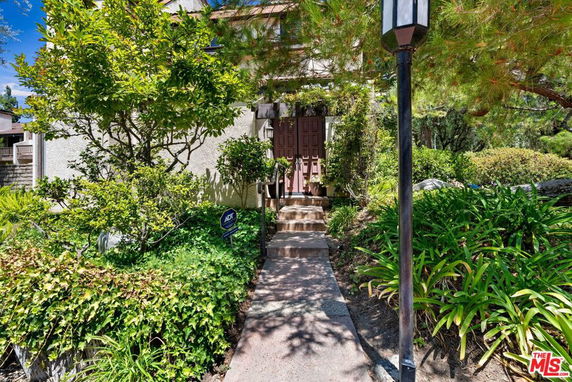 Front view of a house partially obscured by trees and plants.