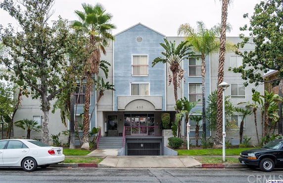 Front view of a multi-story apartment building with an arched entryway and parking ramp.