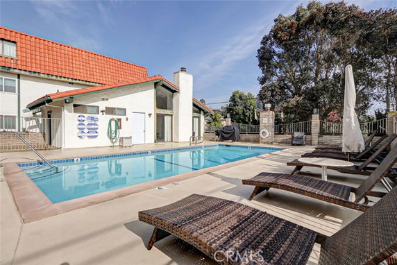 Outdoor swimming pool area with lounge chairs and a building in the background.