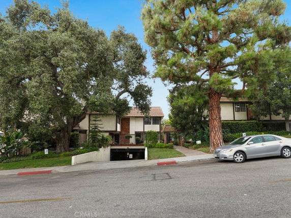 Front view of a residential building with trees and parked cars in the foreground.