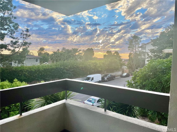 Panoramic view from a building balcony overlooking a street and a sunset sky.