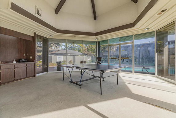 Indoor area with a table tennis setup and large windows overlooking a pool.