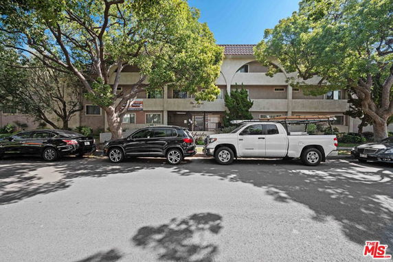 Front view of a multi-story residential building with a tile roof and parking area in front.