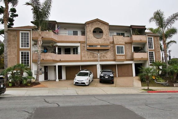 Front view of a multi-story building with balconies and a parking area underneath.