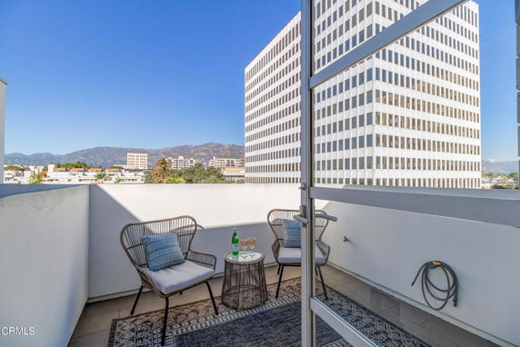 Outdoor seating area on a balcony with view of tall buildings and mountains.