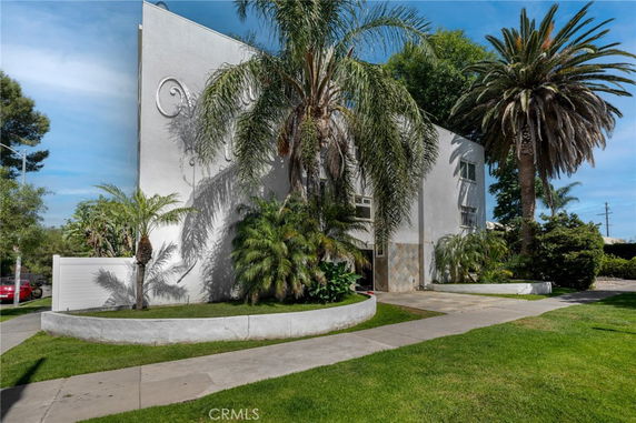 Front view of a multi-story house with a modern facade and palm trees in the front yard.