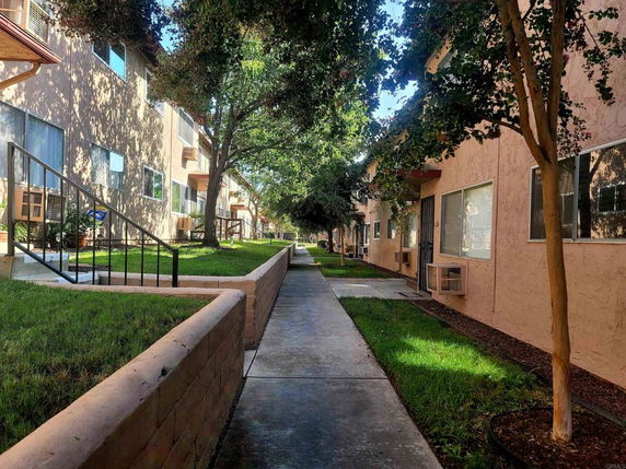 Walkway between residential buildings with trees and grass.