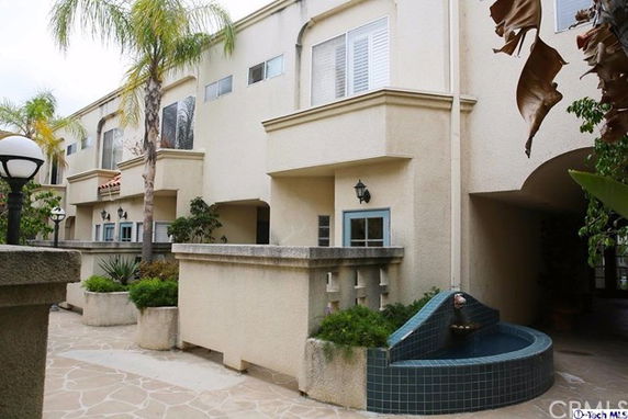 Front view of a multi-story residential building with small balcony areas and decorative fountain.