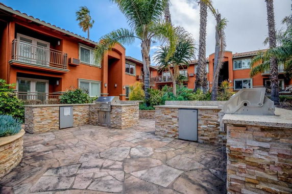 Front view of a multi-story building with balconies and a stone patio area.