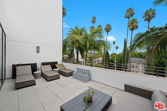Outdoor patio with lounge chairs and railing, overlooking surrounding trees and houses.