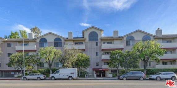 Front view of a multi-story residential building with balconies and trees in front.