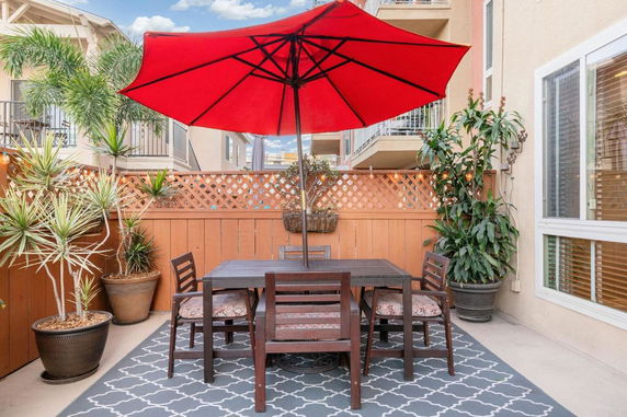 Outdoor patio area with a table, chairs, and a red umbrella.