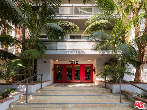 Front view of a multi-story building with palm trees and red doors.