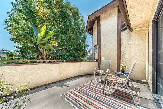 View of a balcony with chairs and a rug overlooking lush green trees from a building.