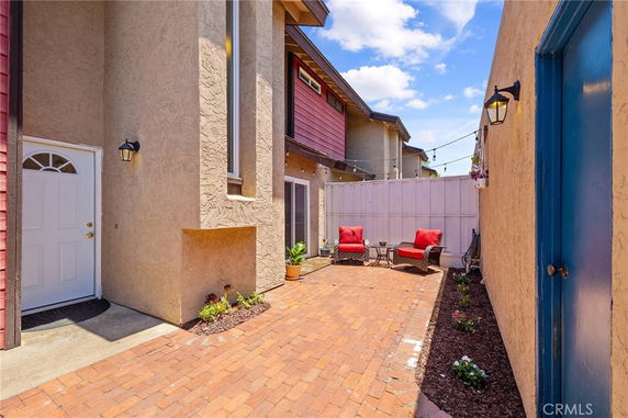 Exterior area with brick pathway between buildings, featuring a white door and patio chairs.