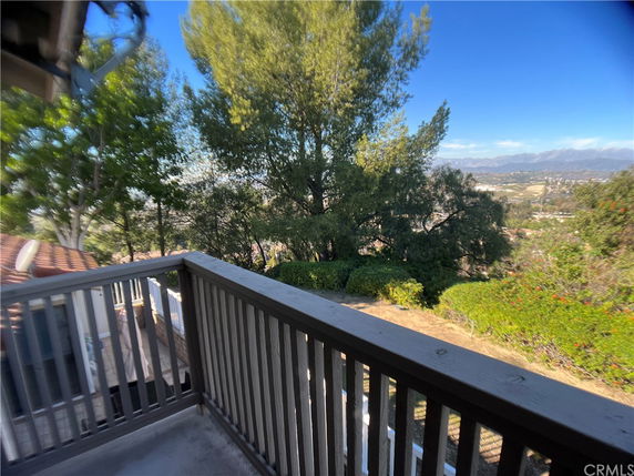 Panoramic view from a balcony overlooking trees and distant hills.