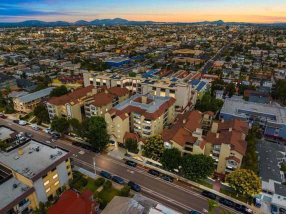 Aerial view of an urban area with residential buildings and streets, showing a complex of multi-story apartments with reddish roofs.