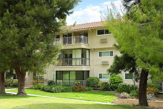 Front view of a multi-story residential building with balconies and surrounded by trees.