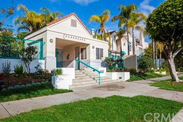 Front view of a residential building with stairs leading to the entrance and palm trees surrounding it.