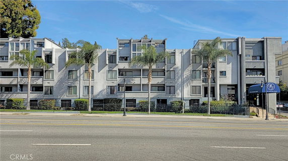 Front view of a multi-story apartment building with palm trees.