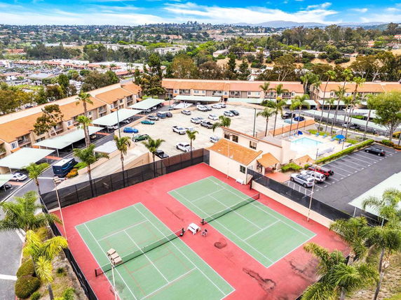 Aerial view of a tennis court adjacent to a residential complex with covered parking.