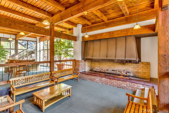 Interior view of a clubhouse with wooden beams, seating area, and a large brick fireplace.