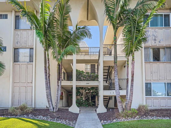 Front view of a multi-story apartment building with balconies and palm trees.