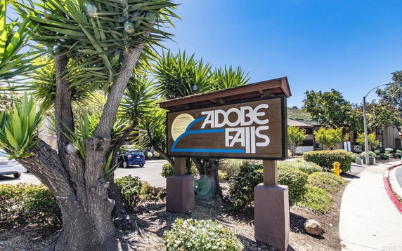 Sign for Adobe Falls with surrounding trees and buildings in the background.