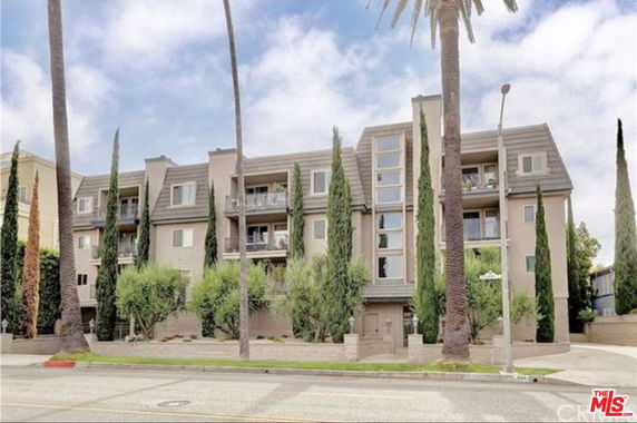 Front view of a multi-story apartment building with balconies and trees.