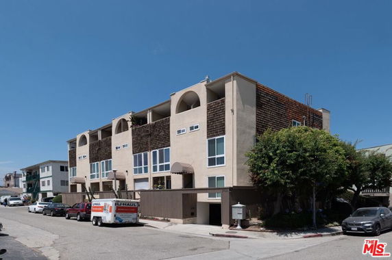 Front view of a multi-story apartment building with balconies and a parking area on the ground floor.