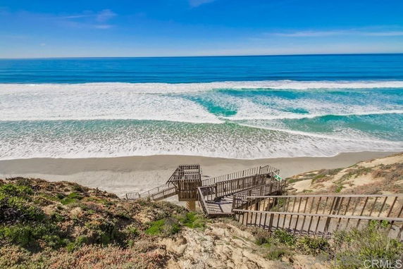Panoramic view of the beach and ocean from a cliff with a wooden staircase leading down to the sand.