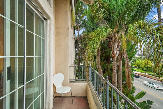 Small balcony with a white chair and view of palm trees and a road.