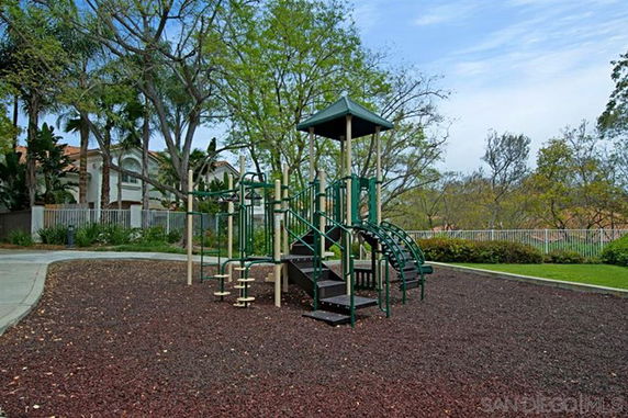 Outdoor play area with a green climbing structure and slide surrounded by trees and grass.