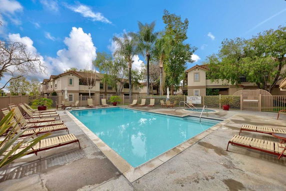 Outdoor swimming pool area with lounging chairs surrounded by residential buildings.